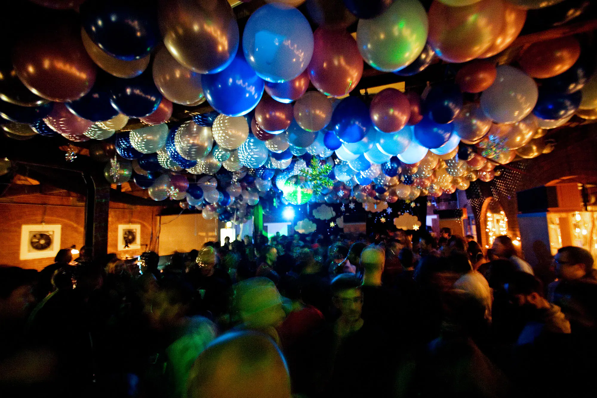 Crowded London loft party beneath silver and blue balloons.